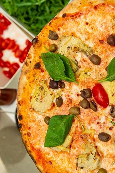 Deliziosa pizza con pomodorini, carciofini, olive e basilico